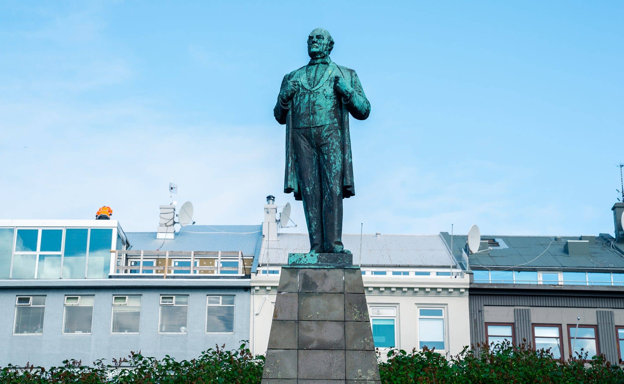 A statue stands against a blue sky above Austurvöllur square in downtown Reykjavík, Iceland.