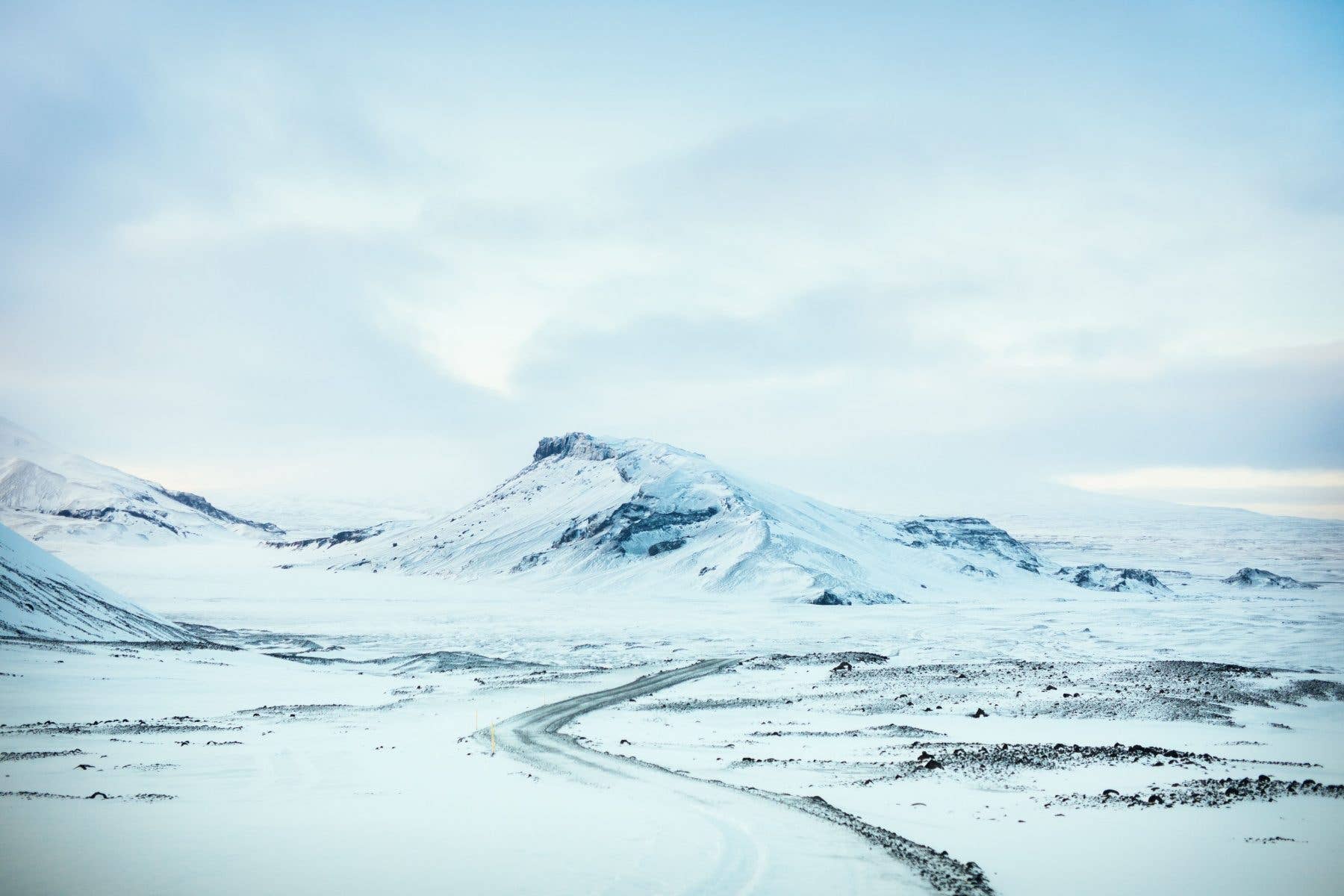 A snowy mountain road leads toward the Langjökull glacier under a winter sky in Iceland.