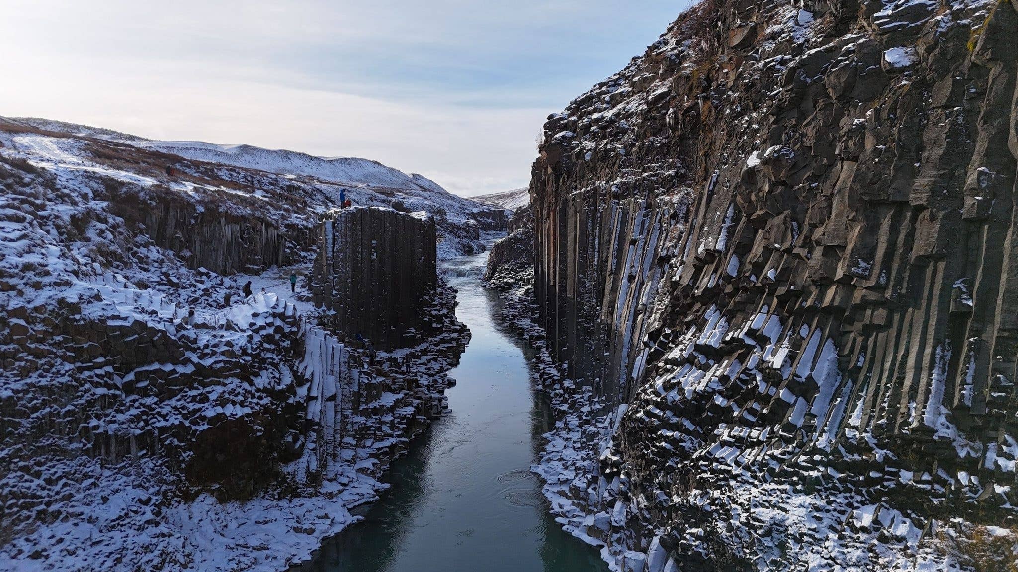 Snow lines the basalt columns and blue river of Stuðlagil canyon in East Iceland.