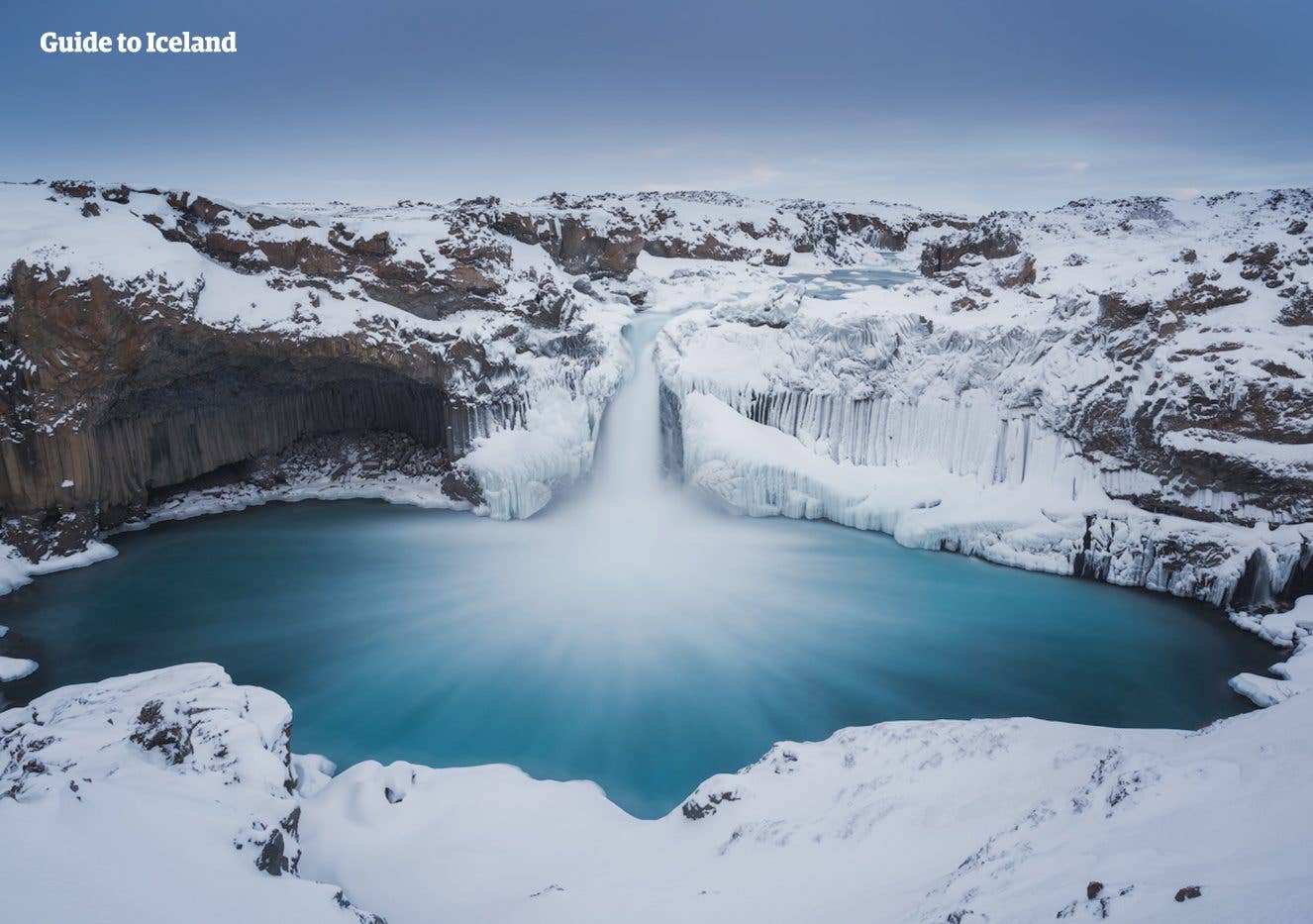 The Aldeyjarfoss waterfall drops between snow-covered basalt columns in the Highlands of Iceland.