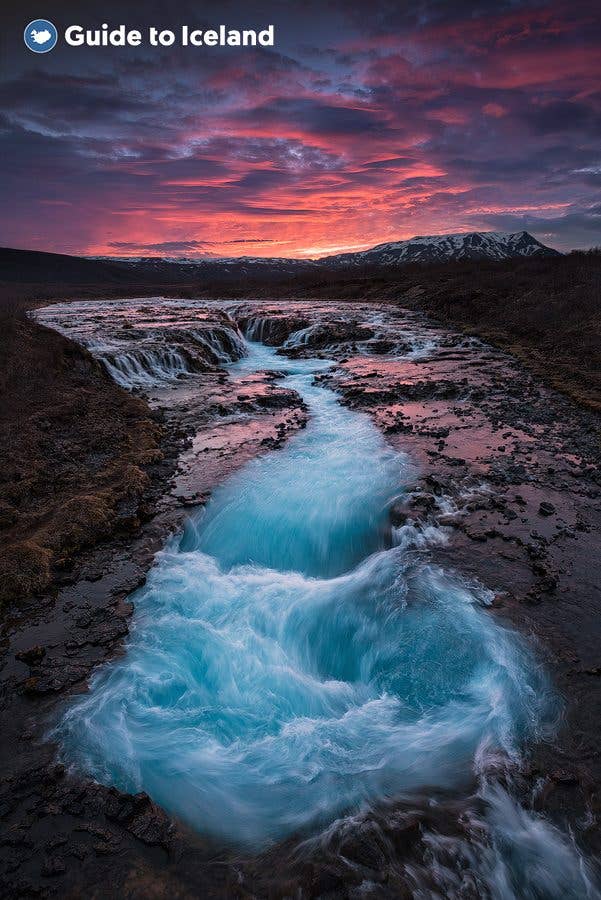 The bright blue water of Brúarfoss waterfall glows under a sunset sky in South Iceland.