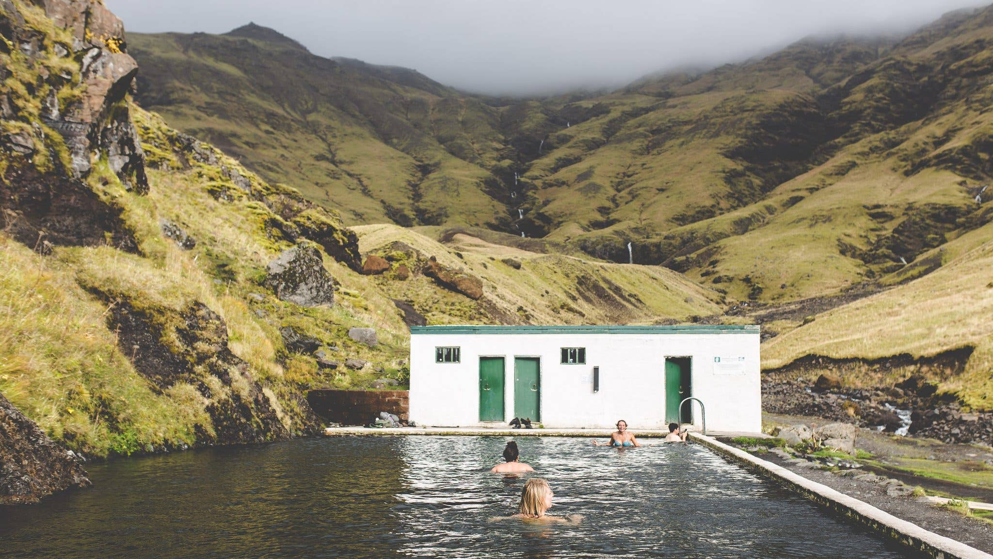 The historic Seljavallalaug pool sits in a green valley beneath the mountains of South Iceland.