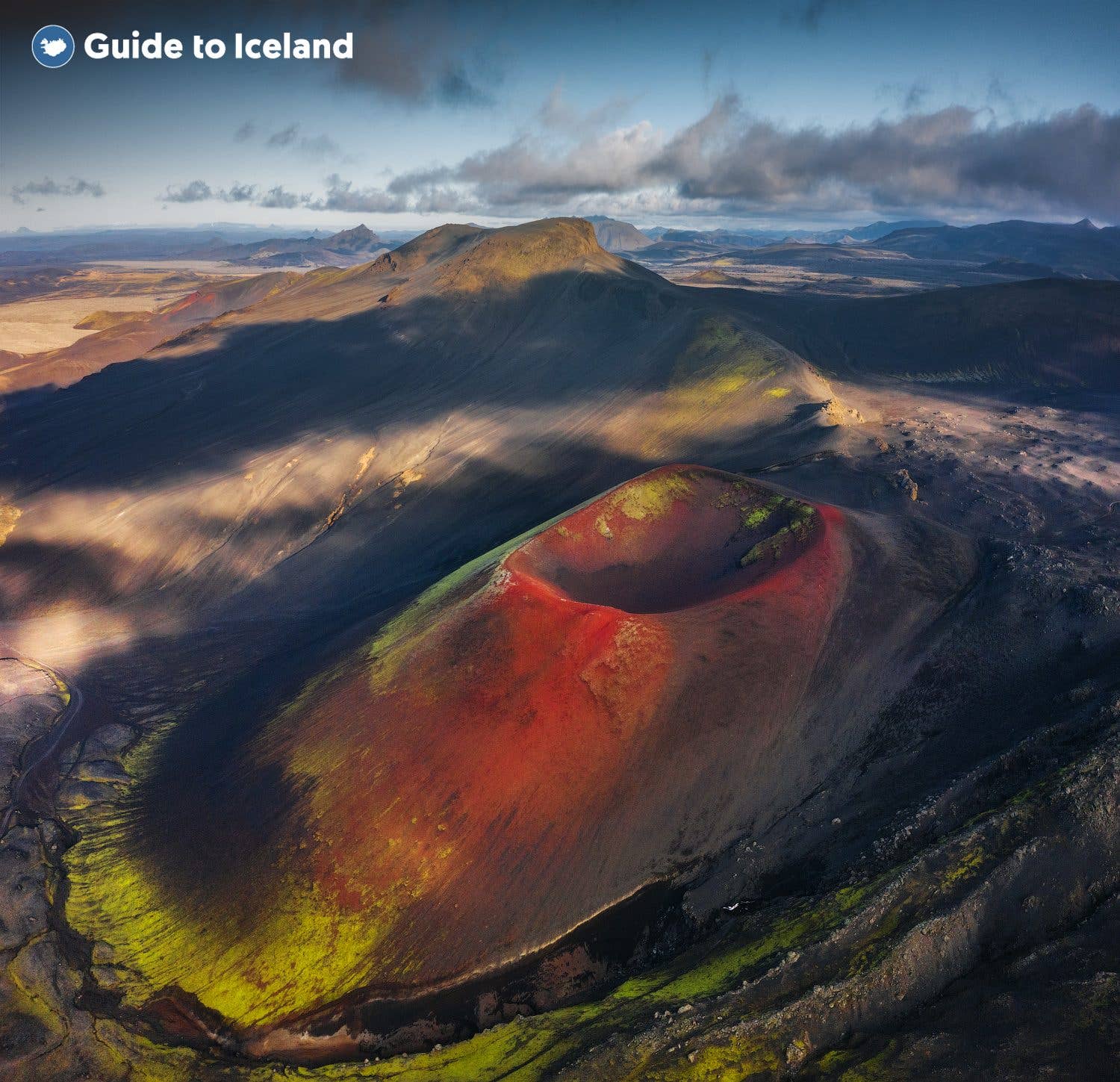 A red volcanic crater rises from the green highlands near Landmannalaugar in Iceland.