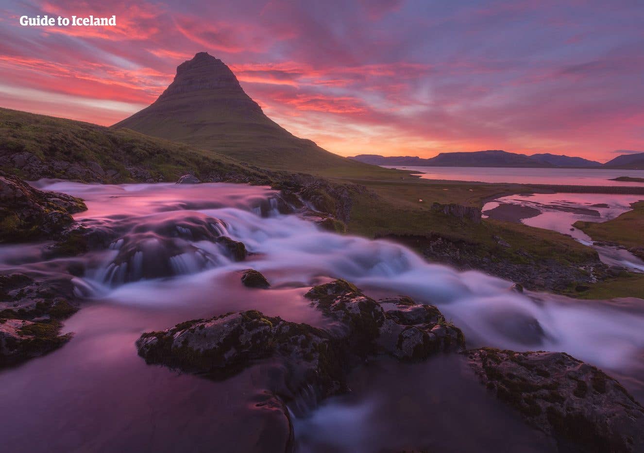 A pink sunset glows behind Kirkjufell mountain and its waterfall on the Snæfellsnes Peninsula, Iceland.