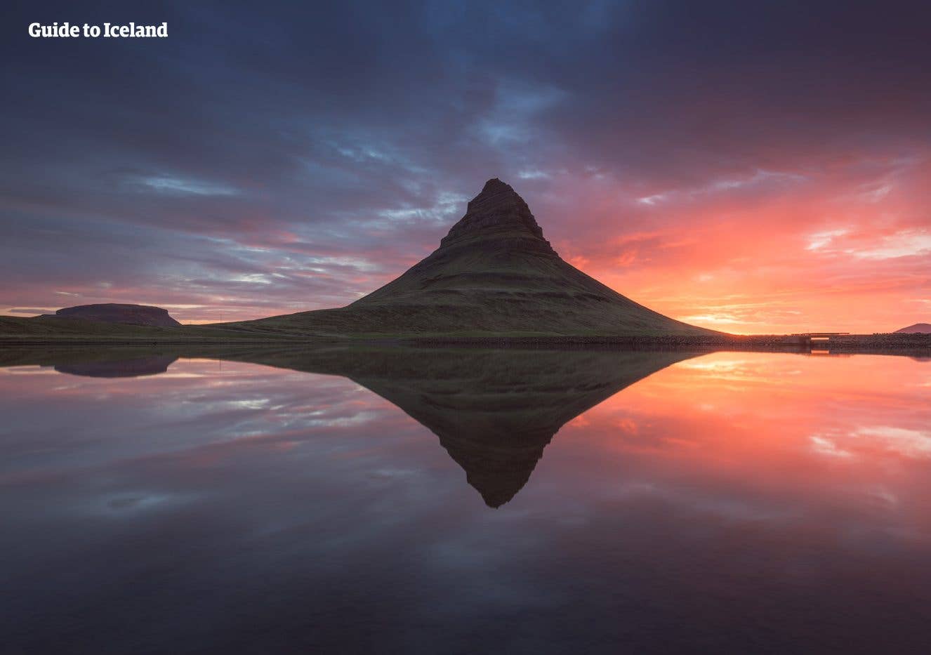Kirkjufell mountain reflects in still water under an evening sky on the Snæfellsnes Peninsula, Iceland.