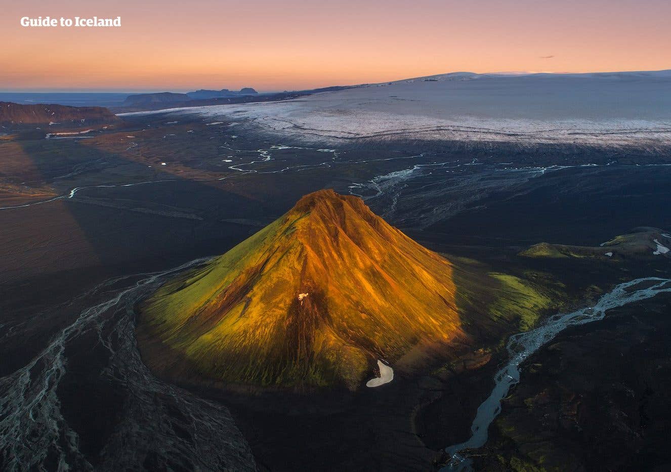 The green cone of Mælifell rises from black sands below a glacier in the Icelandic highlands.