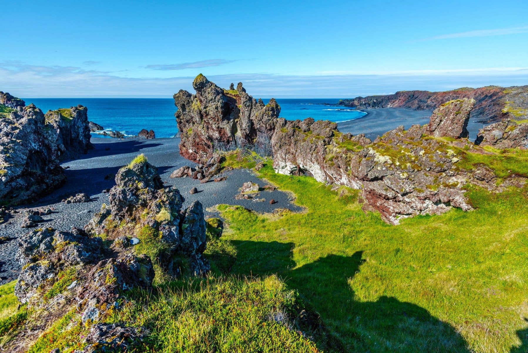 Jagged lava rocks and green slopes meet the sea at Djúpalónssandur on the Snæfellsnes Peninsula, Iceland.