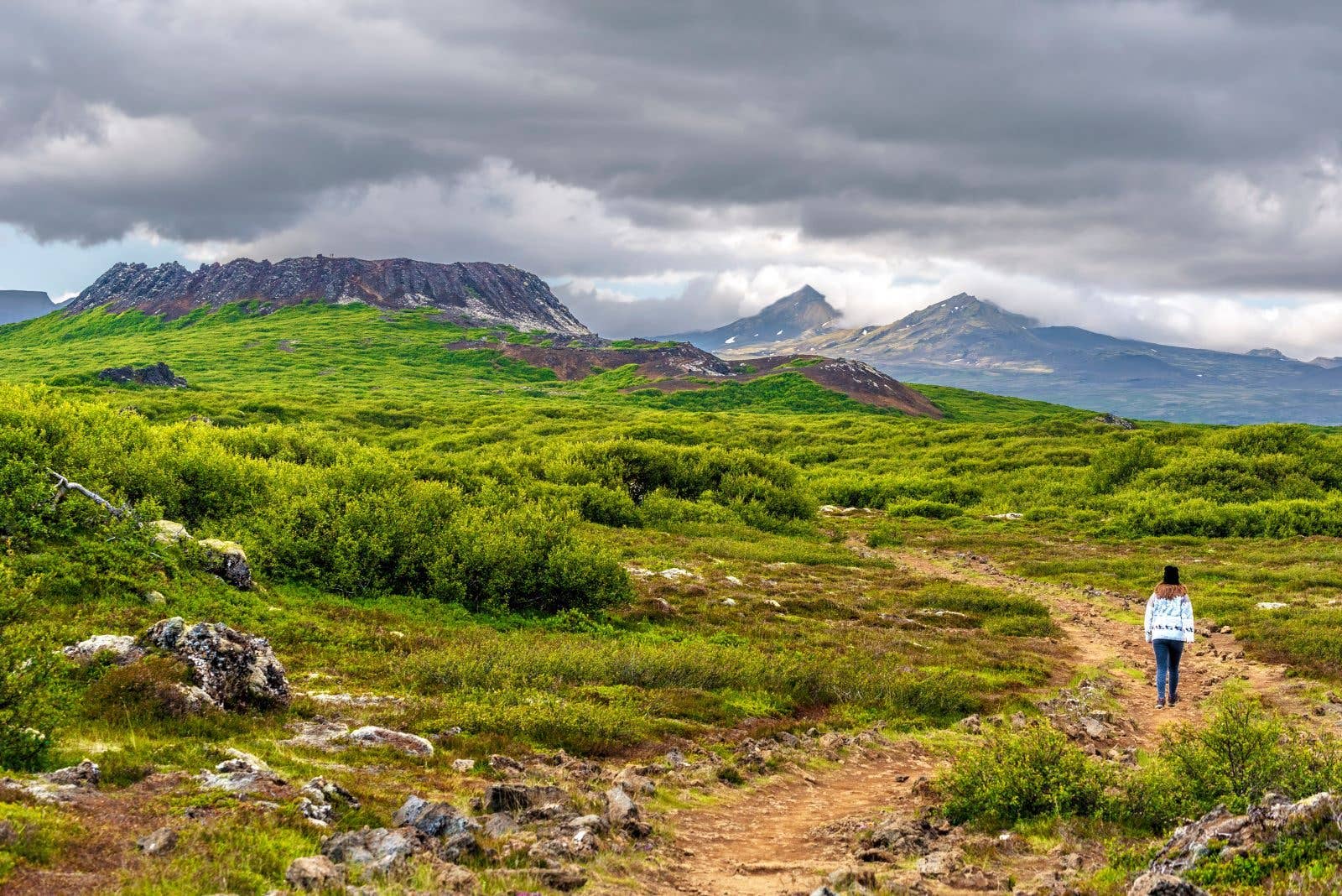 A hiker walks toward the Eldborg crater across the green lowlands of the Snæfellsnes Peninsula, Iceland.