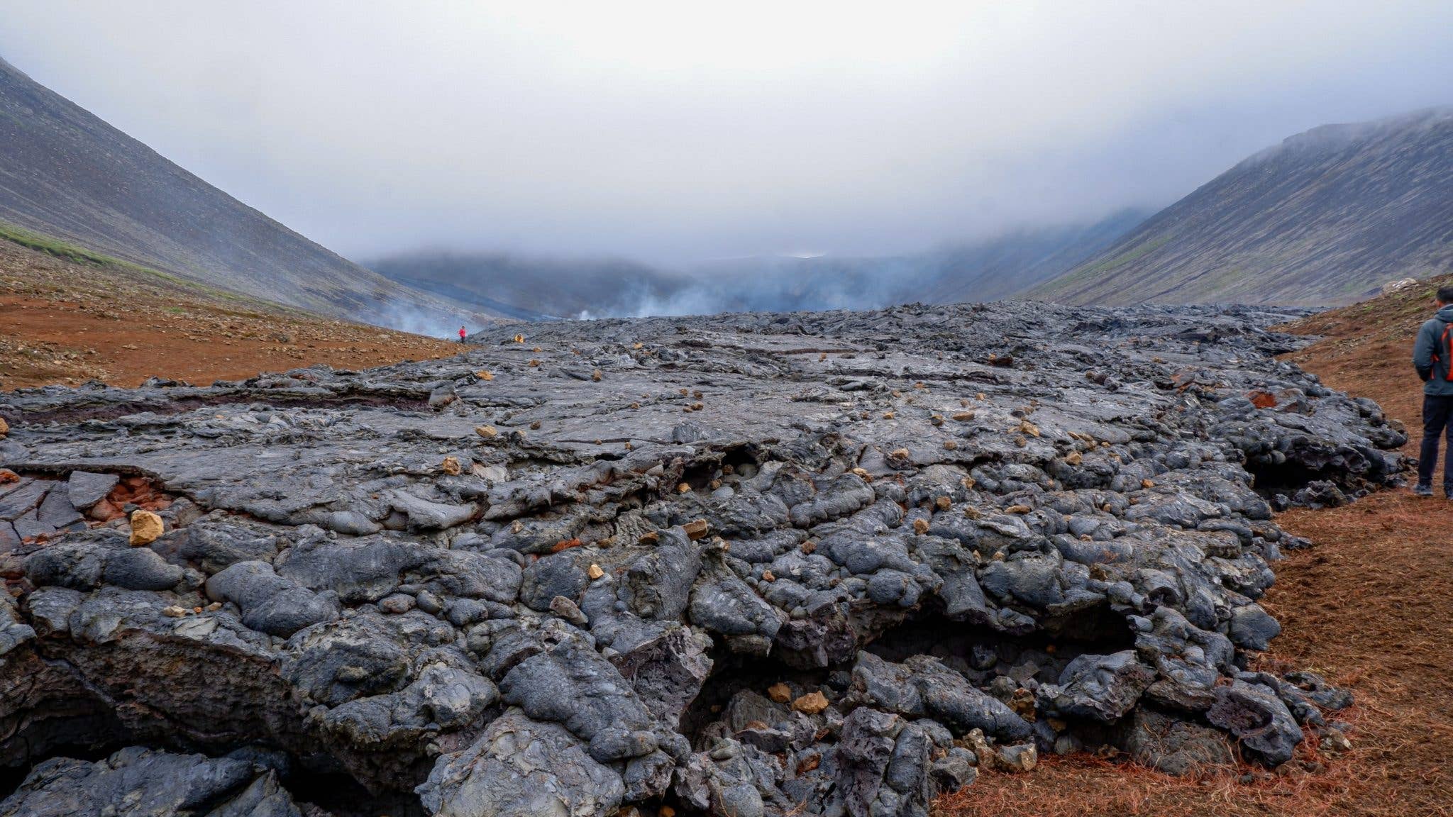 A hiker crosses the fresh lava field near Fagradalsfjall on the Reykjanes Peninsula in Iceland.