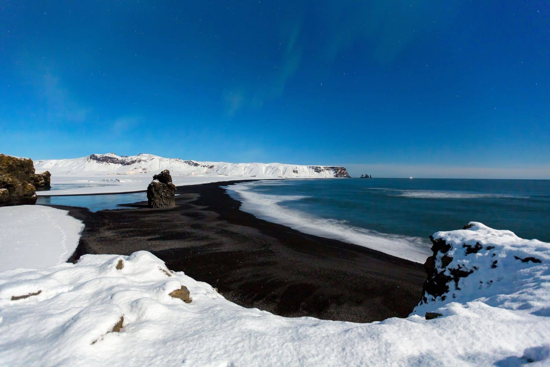 Snow dusts the black sands of Reynisfjara beach seen from above on the south coast of Iceland.