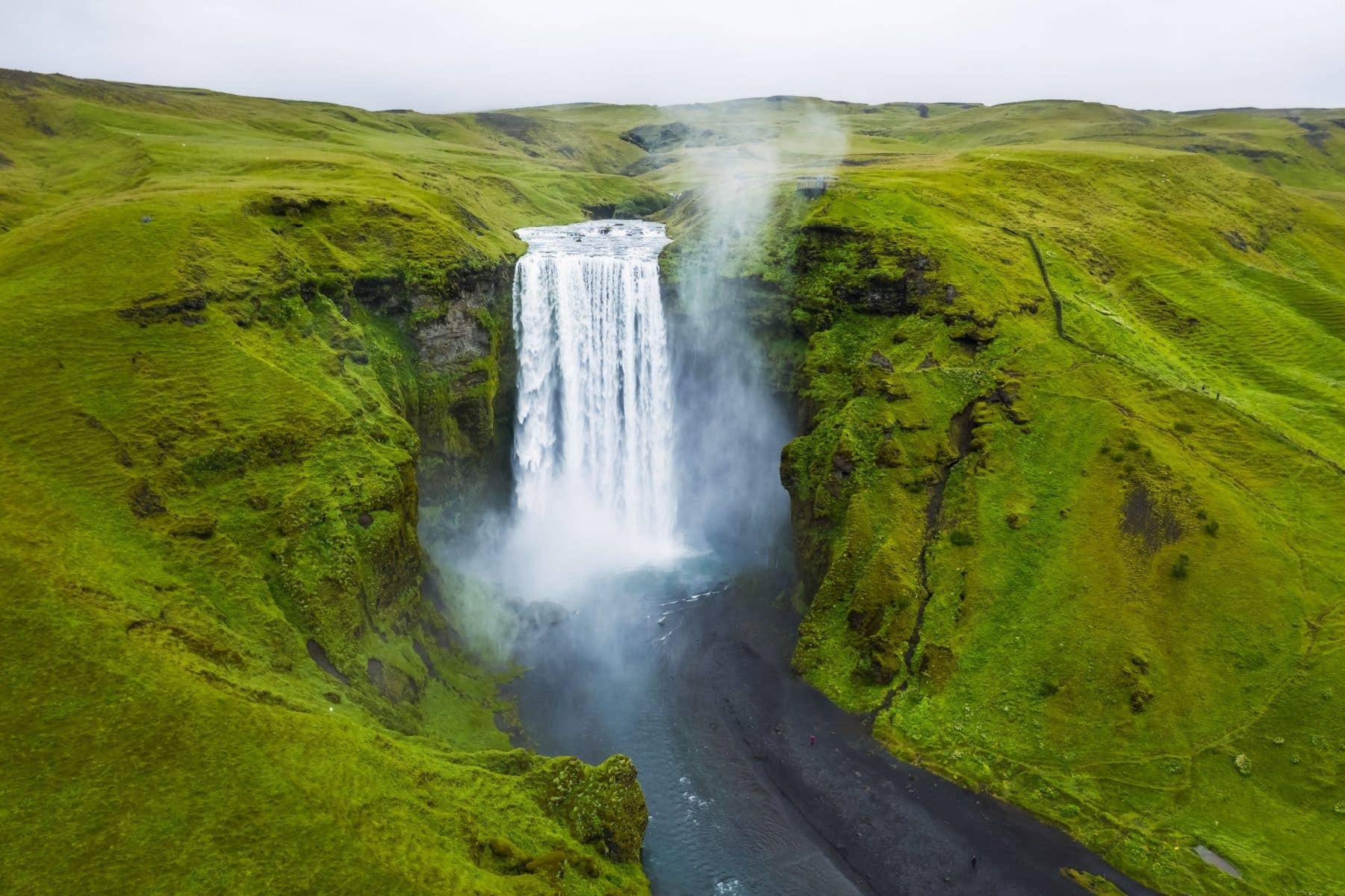 The Skógafoss waterfall pours between bright green summer hills in South Iceland.