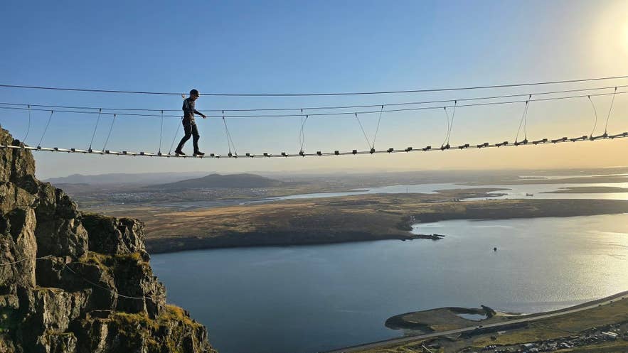 Climber clipped into the steel cables of the Falkaklettur via ferrata route on Mount Esja near Reykjavik, with views over the coastline.