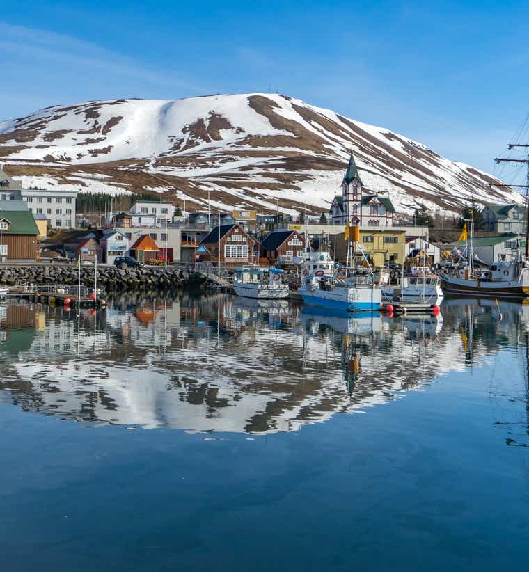 Husavik Harbor with colorful fishing boats and snow-capped mountains in North Iceland.