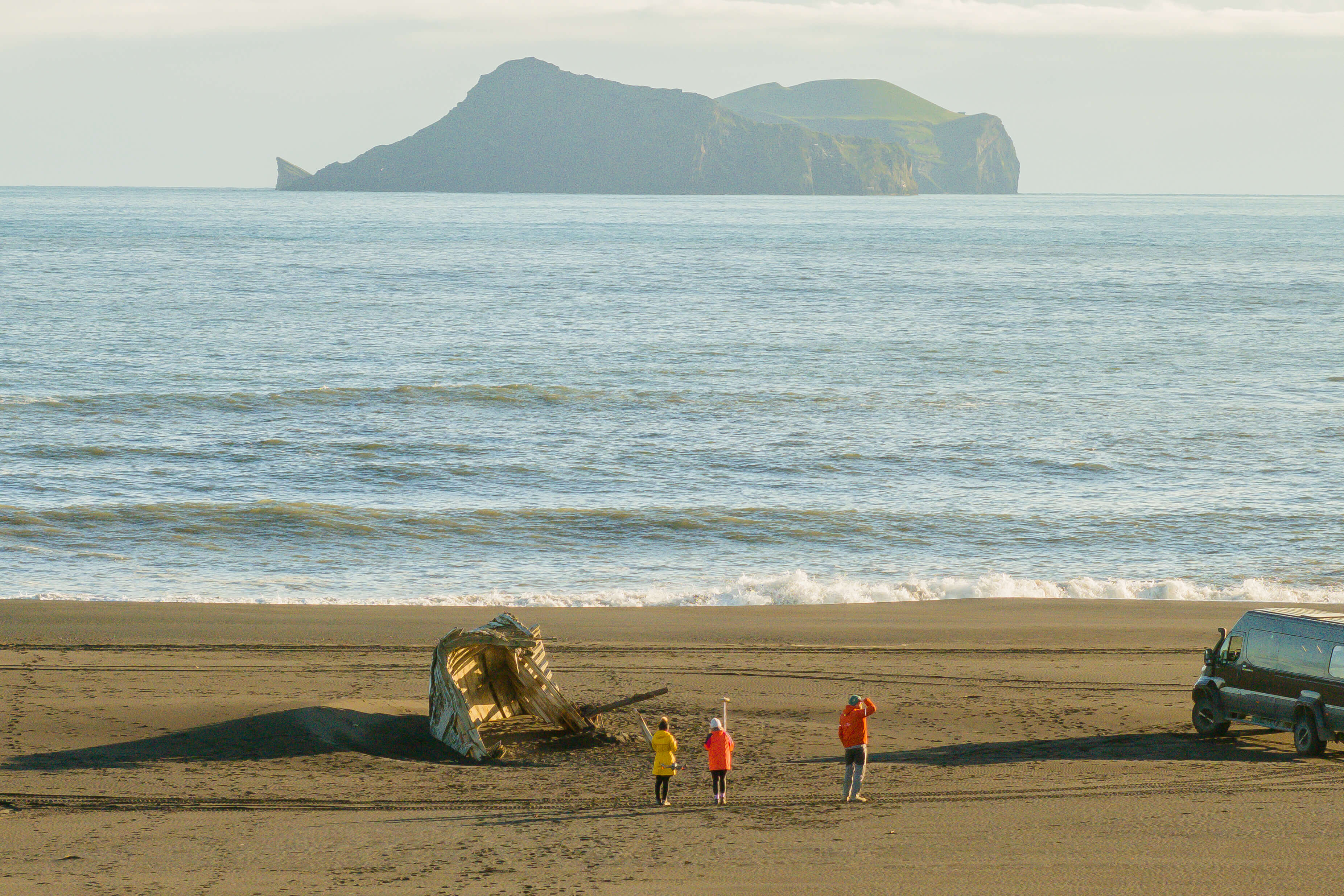 Researchers in orange safety gear take GPS measurements on the black sand of Landeyjasandur Beach in South Iceland.