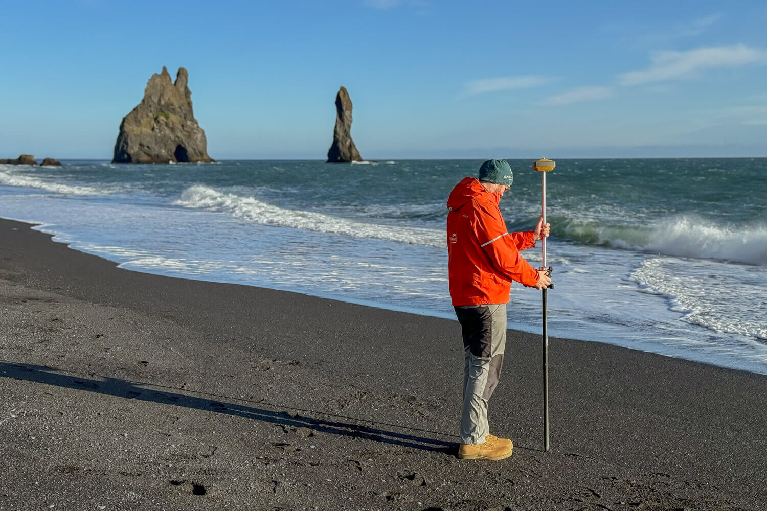 A participant uses surveying equipment to collect coastal data along Reynisfjara Black Sand Beach.