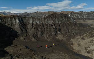 Three travellers stand below the ash-covered ice wall of Kotlujokull Glacier with Myrdalsjokull Glacier beyond.