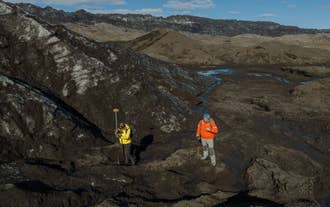 Two travelers record GPS readings on the ash-streaked ice of Katla Glacier during a citizen science mapping expedition.