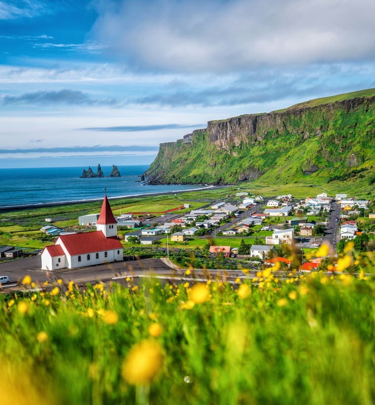 Vik Village on Iceland's South Coast in summer with a black sand beach and the Reynisdrangar Sea Stacks beyond