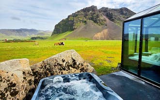 Outdoor hot tub beside a glass cabin looks out over green fields toward the Eyjafjoll Mountains.