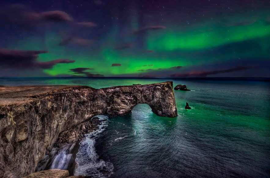 Green northern lights above the sea arch at Dyrholaey Cliffs on the South Coast of Iceland