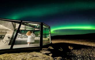 Guest in a robe watches the northern lights from the glass front of a cabin near Hvolsvollur.