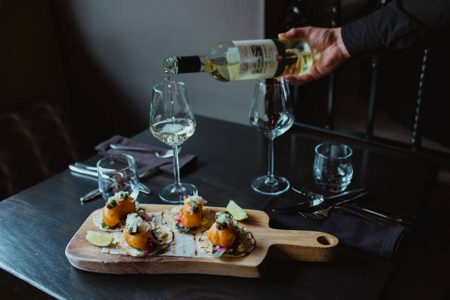 Langoustine tacos served on a wooden board at Sjávargrillið as a glass of white wine is poured.
