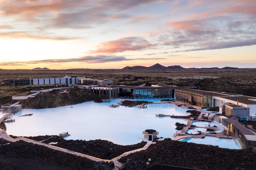 Aerial view of Blue Lagoon Geothermal Spa glowing milky blue under a pink sunset sky on the Reykjanes Peninsula.