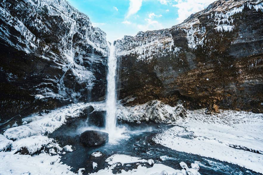 Kvernufoss waterfall falling between ice-covered cliffs in winter in South Iceland.