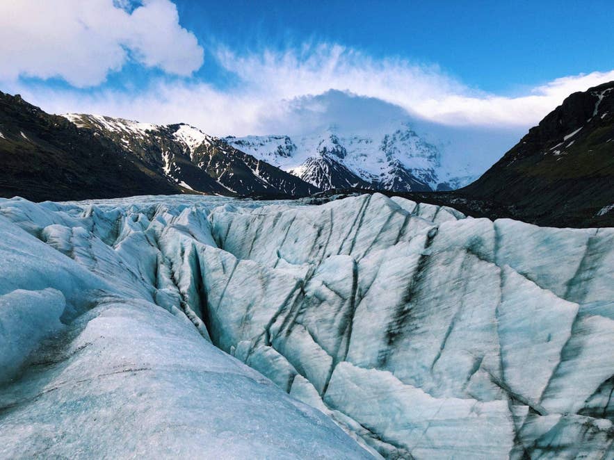 A glacier tongue flowing between dark mountains in Iceland under a blue sky