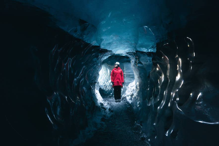 A person in a red jacket standing inside a blue ice cave in Iceland