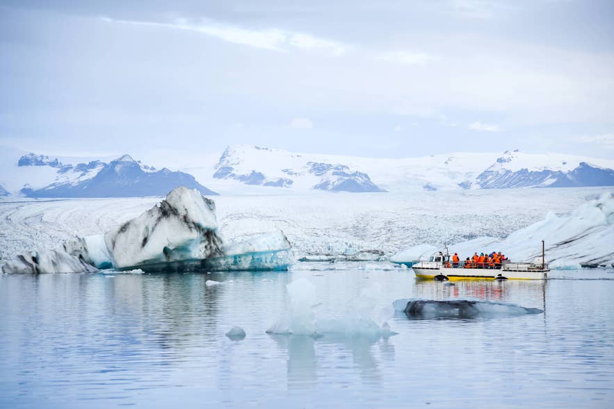 A boat of travelers in orange life jackets passing icebergs in a glacier lagoon in Iceland