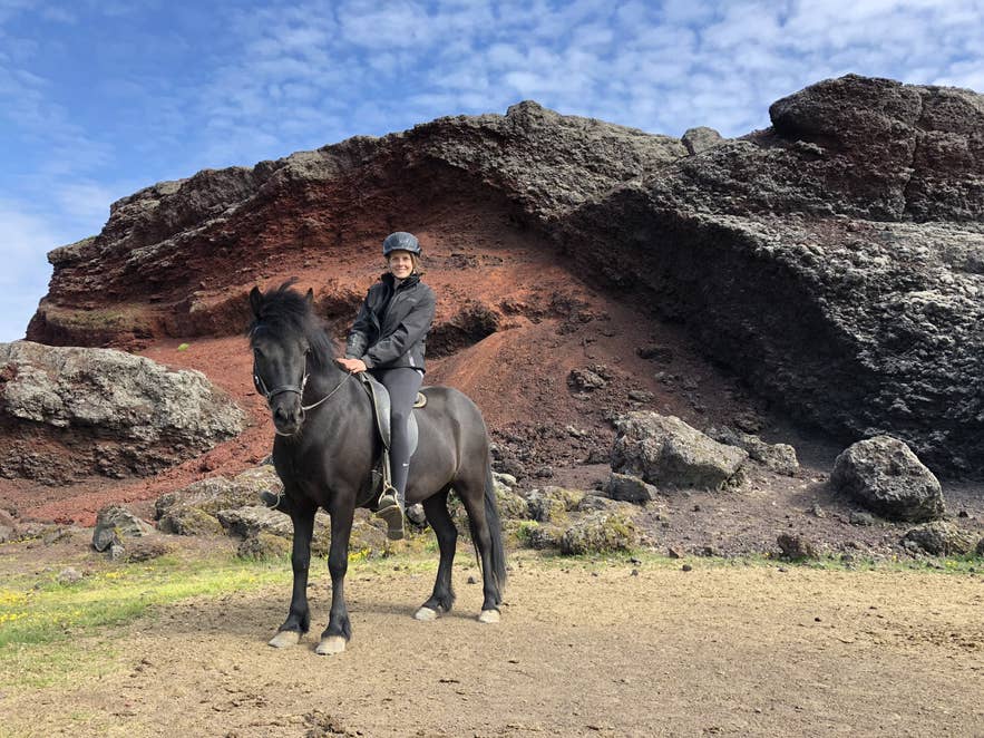 Rider on a black Icelandic horse beside red and black volcanic rock