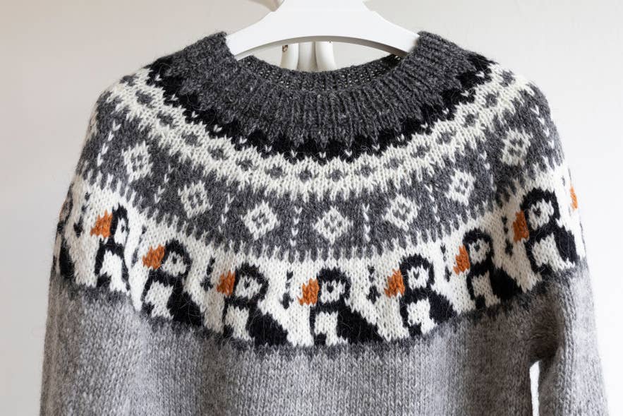 Gray Icelandic lopapeysa sweater on a hanger, with a row of knitted puffins below the patterned yoke. Gray Icelandic lopapeysa sweater on a hanger, with a row of knitted puffins below the patterned yoke.