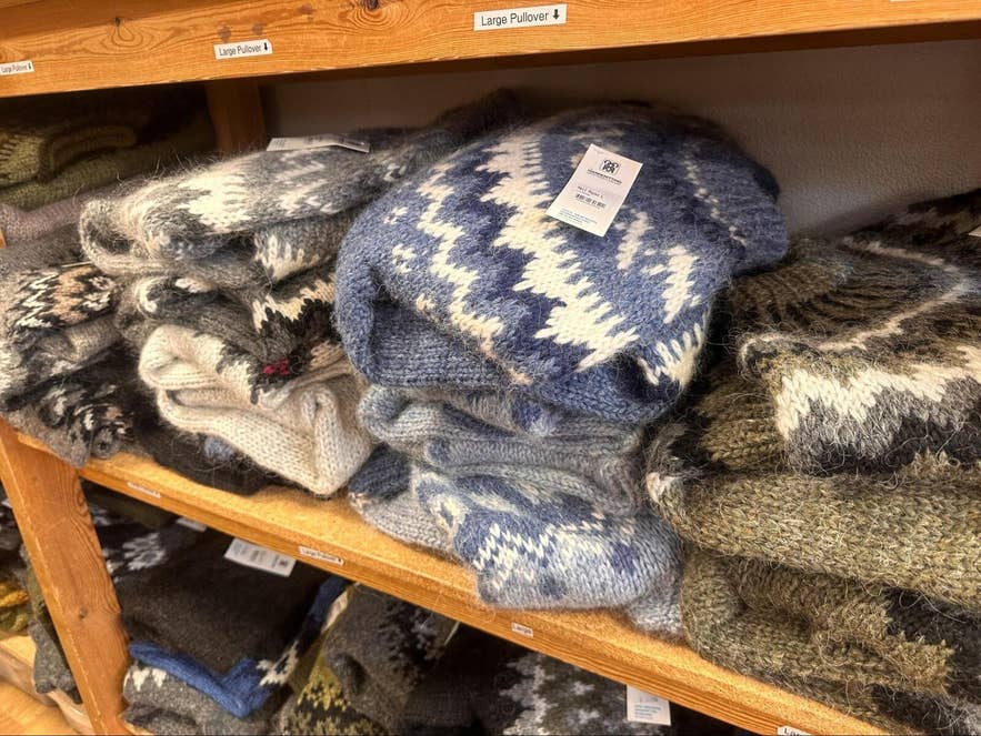 Folded Icelandic wool sweaters stacked on wooden shop shelves, with price tags and size labels. Folded Icelandic wool sweaters stacked on wooden shop shelves, with price tags and size labels.