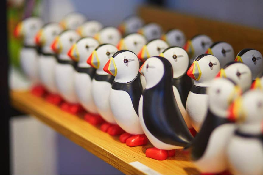 A row of painted wooden puffin figurines lined up on a shop shelf. A row of painted wooden puffin figurines lined up on a shop shelf.