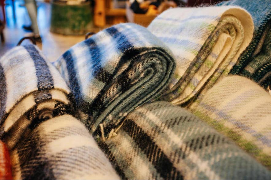 Rolled Icelandic wool blankets in blue, green, and cream plaid, stacked in a shop. Rolled Icelandic wool blankets in blue, green, and cream plaid, stacked in a shop.
