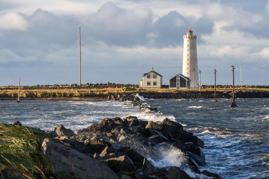 Grotta Island Lighthouse and its white house behind waves breaking over a rocky shore. Grotta Island Lighthouse and its white house behind waves breaking over a rocky shore.