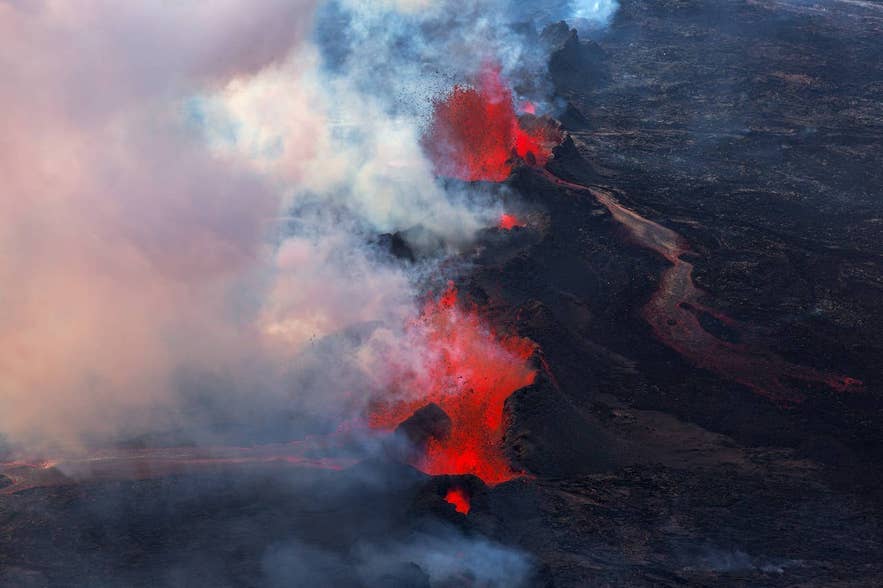 Bright red lava fountains and steam rising from an erupting fissure over a dark lava field in Iceland