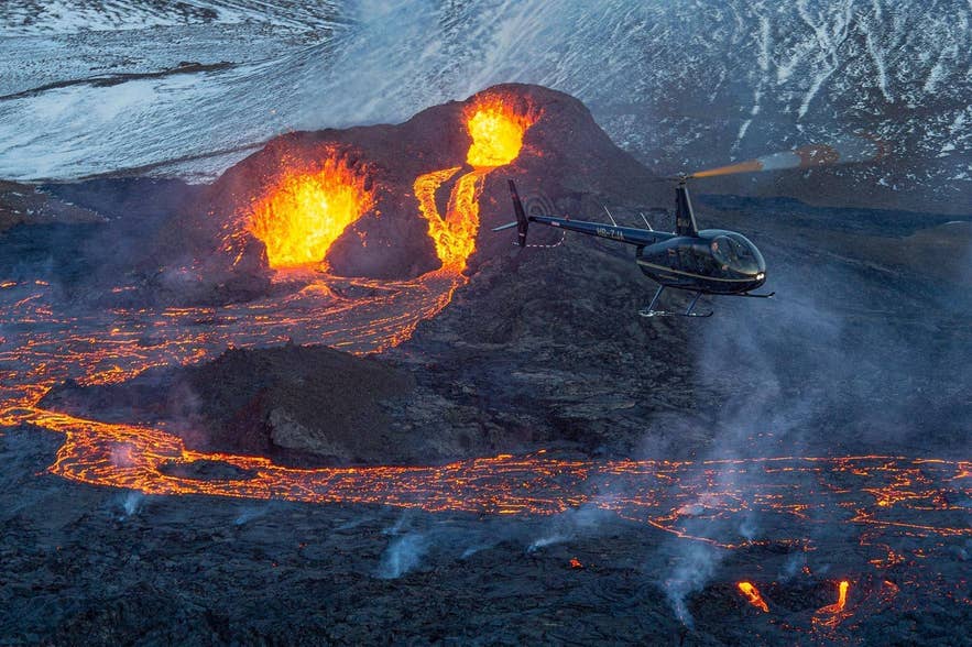 Helicopter flying close to erupting craters and rivers of glowing lava during an eruption in Iceland
