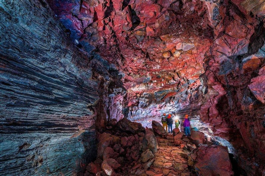 Travelers walking through a lava tunnel with red and blue mineral colored walls in Iceland