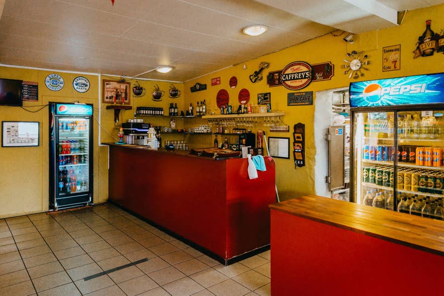 Counter and drinks fridges inside Gallery Pizza in Hvolsvollur, with yellow walls and framed memorabilia.