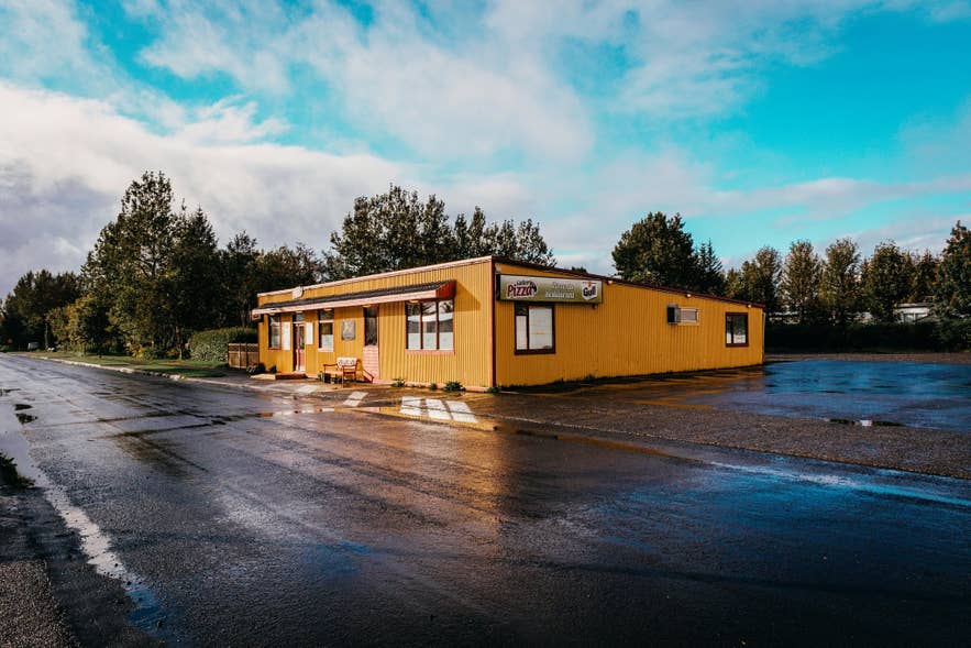 Yellow exterior of Gallery Pizza beside a wet car park in Hvolsvollur on Iceland's South Coast.