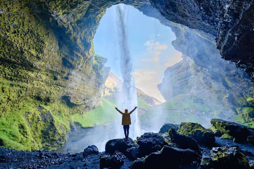 Visitor standing behind Seljalandsfoss waterfall on Iceland’s South Coast.