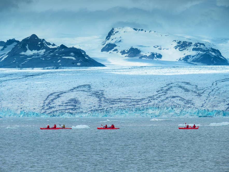 Kayakers paddle in a glacier lagoon beneath a snow-capped glacier in Iceland Kayakers paddle in a glacier lagoon beneath a snow-capped glacier in Iceland