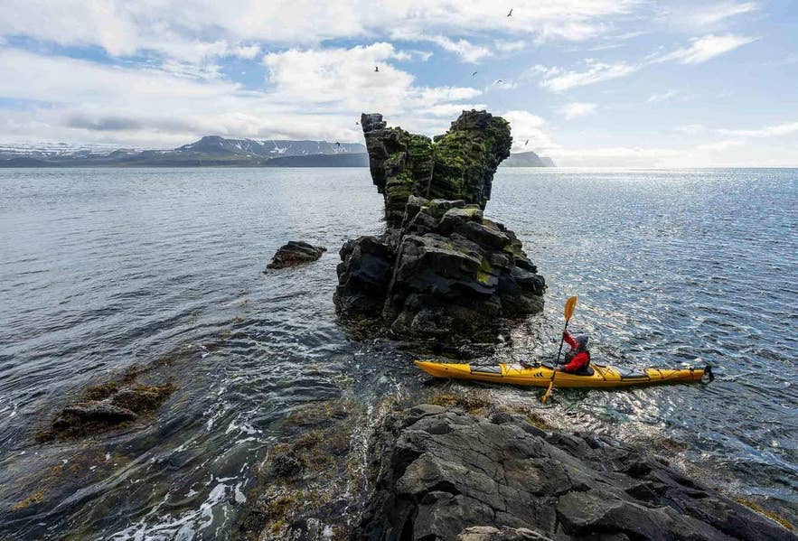 A sea kayaker paddles past a rocky sea stack on the Icelandic coast A sea kayaker paddles past a rocky sea stack on the Icelandic coast