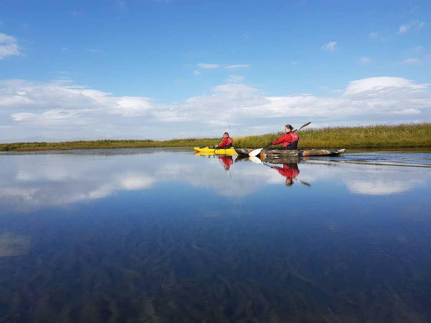 Two kayakers glide across a still, reflective lake in Iceland Two kayakers glide across a still, reflective lake in Iceland