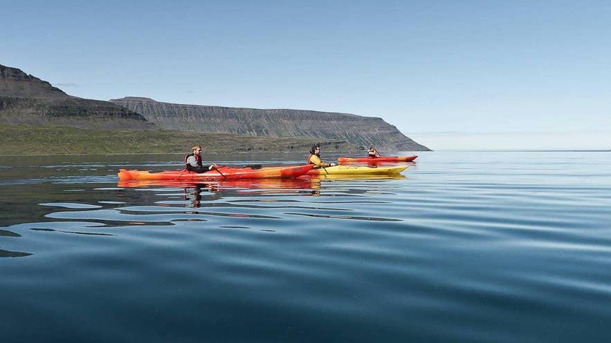 A group of kayakers crosses a calm fjord on a clear summer day in Iceland A group of kayakers crosses a calm fjord on a clear summer day in Iceland