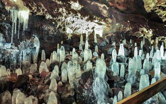 Clusters of pale ice stalagmites rise from the floor of Vidgelmir Lava Cave beside the boardwalk.