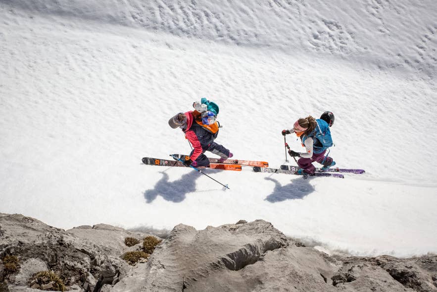 Two backcountry skiers descending a steep snowy slope in Iceland.