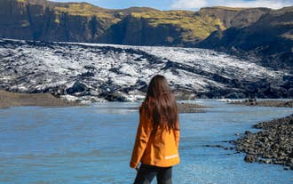 A traveler in an orange jacket looks out over the ice front of Solheimajokull Glacier on the South Coast of Iceland.